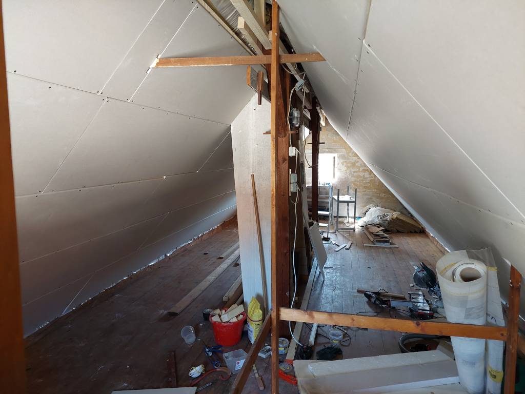 Der Ausbau des Dachbodens zum Lager im Rohbau. Gipsplatten sind an der Decke. Die Dämmarbeiten sind beendet.